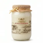 Glass jar of Urban Organic Ghritam A2 Arjun Chhaal Ghee featuring a traditional rural Bilona churning illustration